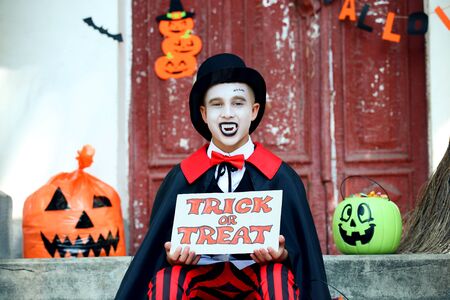 Young boy in halloween costume holding paper with text Trick or Treatの写真素材