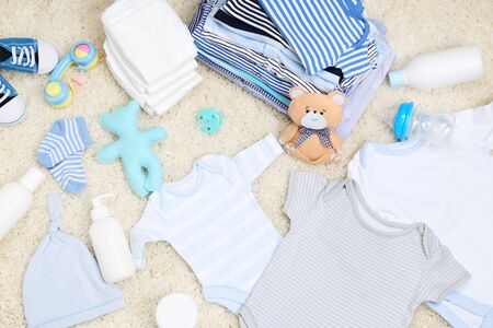 Baby clothes with toys and diapers on carpetの写真素材