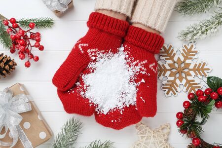 Hands in knitted mittens holding white snow with christmas ornaments on wooden tableの写真素材