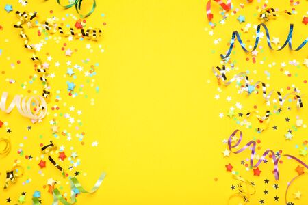 Colorful ribbons with paper stars and confetti on yellow backgroundの写真素材