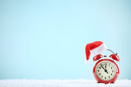 Red alarm clock with santa hat on blue background