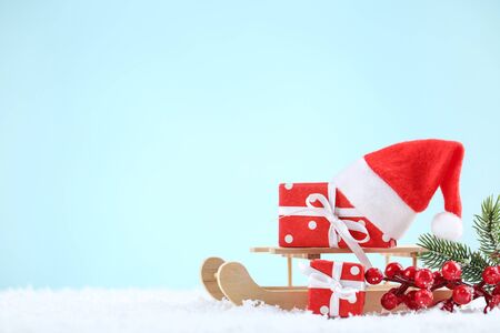 Red santa hat with gift boxes, red berries and wooden sleigh on blue background
