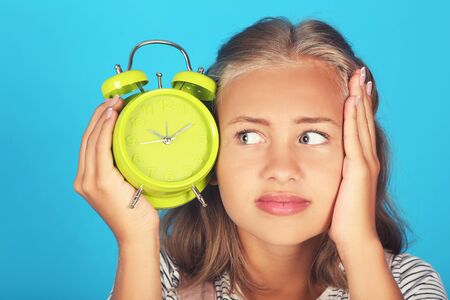 Young girl holding green alarm clock on blue backgroundの写真素材