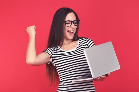 Young girl in eyeglasses with laptop computer on red backgroundの写真素材