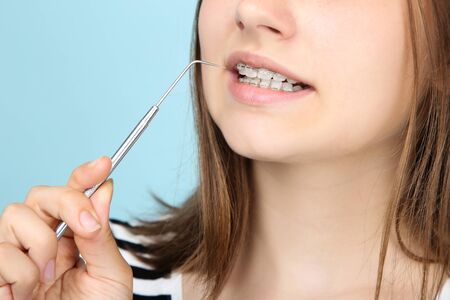 Young girl with dental braces holding dentist tool on blue background