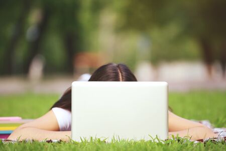 Young girl with laptop computer lying on the grass in parkの写真素材