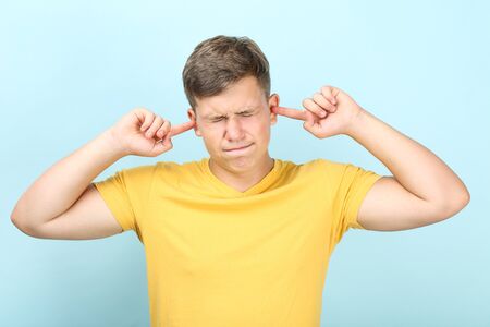 Young man closing ears by fingers on blue backgroundの写真素材