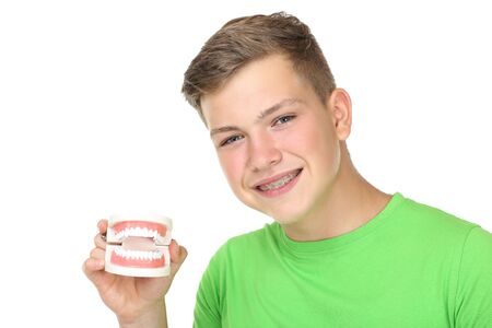 Young man with dental braces holding teeth model on white background
