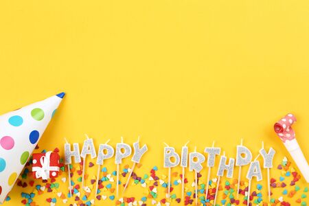 Happy Birthday candles with party decorations and sprinkles on yellow backgroundの写真素材