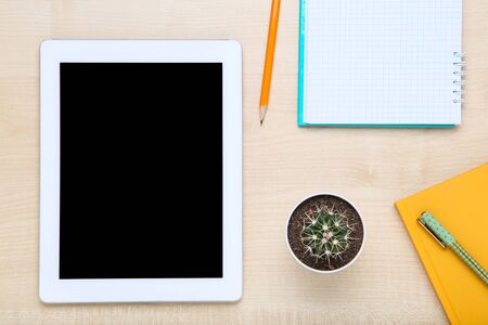 Tablet computer with notepads and cactus on brown wooden table