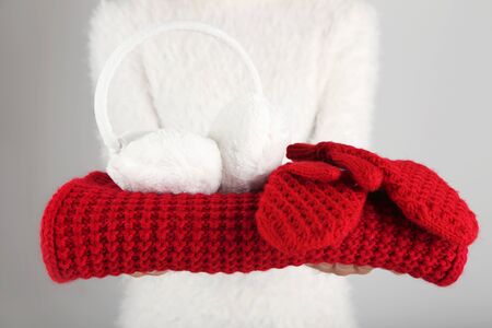 Female hands holding knitted scarf, pair of gloves and earmuffs on grey background