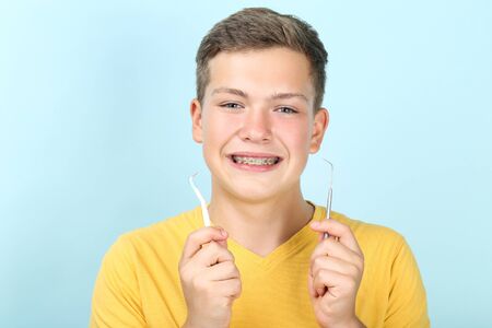 Young man with toothbrush and dentist tool on blue background