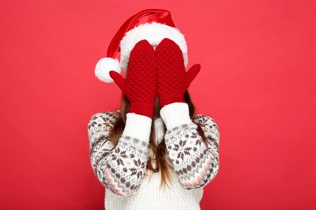 Beautiful woman wearing sweater, gloves and santa hat on red backgroundの写真素材