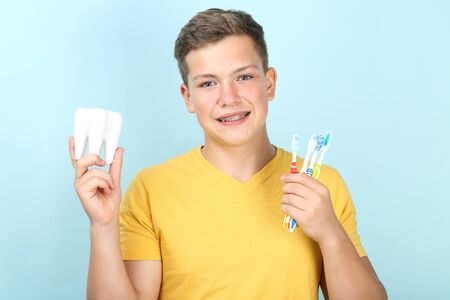 Young man with toothbrushes and tooth model on blue background