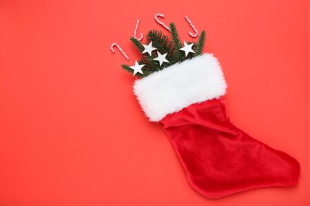 Red christmas stocking with fir tree branches, stars and candy canes on red background