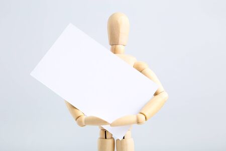 Wooden figure holding blank business card on grey backgroundの写真素材