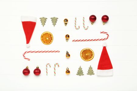 Flat lay christmas composition. Ornaments, candies and santa hats on white wooden tableの写真素材