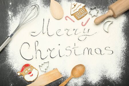 Text Merry Christmas on flour with cookies and kitchen utensilsの写真素材