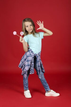 Young girl in fashion clothing with lollipops on red backgroundの写真素材