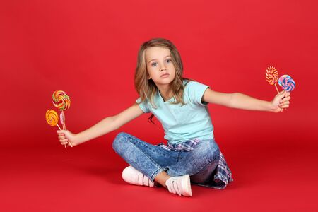 Young girl with colorful lollipops on red backgroundの写真素材