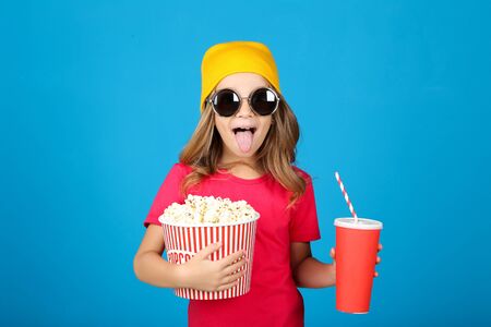 Young girl with popcorn in bucket and paper cup on blue backgroundの写真素材