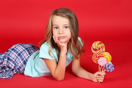 Young girl with colorful lollipops on red backgroundの写真素材
