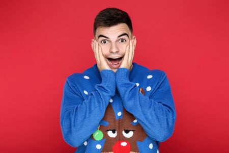 Beautiful man in blue christmas sweater on red background