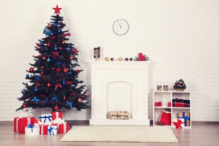 Christmas fir tree with ornaments and gift boxes near decorated fireplace at homeの写真素材
