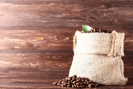 Coffee beans in sackcloth with green leaf on wooden tableの写真素材