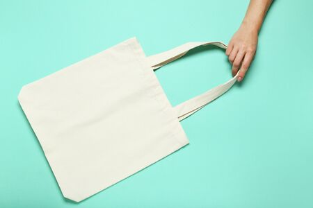 Female hand holding white cotton eco bag on mint background