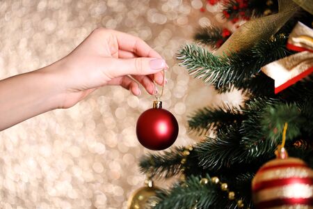 Female hand decorating christmas fir tree on blurred lights backgroundの写真素材