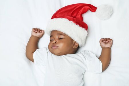 American baby girl in santa hat sleeping on white bed