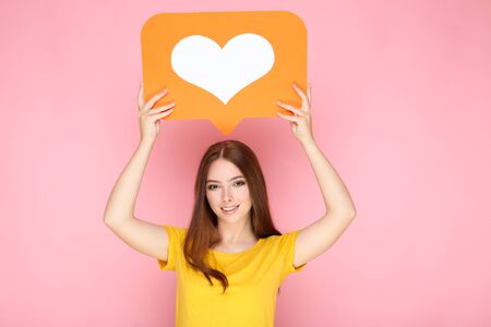 Young woman holding paper card with heart on pink background