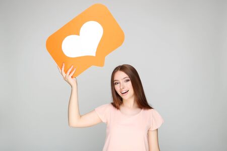 Young woman holding paper card with heart on grey background
