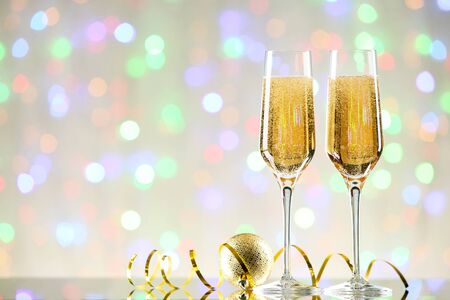 Glasses of champagne with bauble and ribbon on blurred lights backgroundの写真素材
