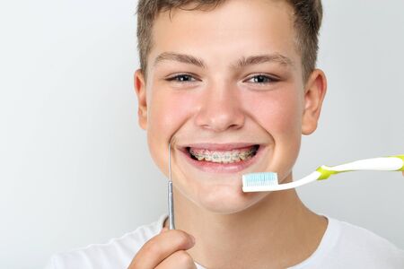 Young man with toothbrush and dentist tool on grey backgroundの写真素材