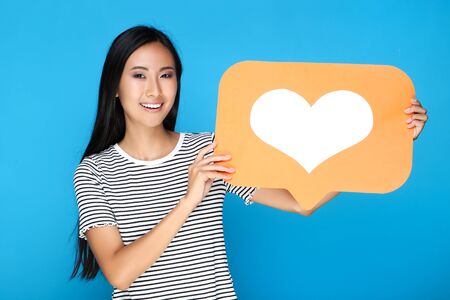Beautiful woman holding paper card with heart on blue backgroundの写真素材