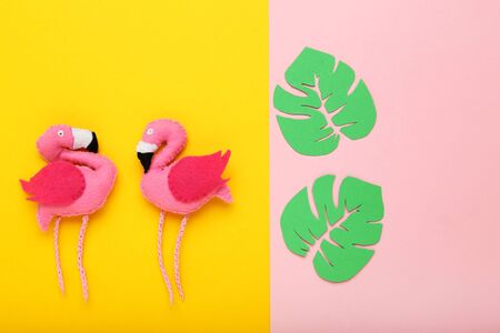 Soft toy of flamingos with green paper leafs on colorful paper backgroundの写真素材
