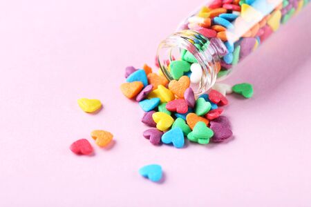 Colorful heart shaped sprinkles with glass bottle on pink backgroundの写真素材