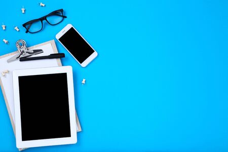 Tablet computer with smartphone, glasses and clipboard on blue backgroundの写真素材