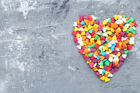 Colorful heart shaped sprinkles on grey background