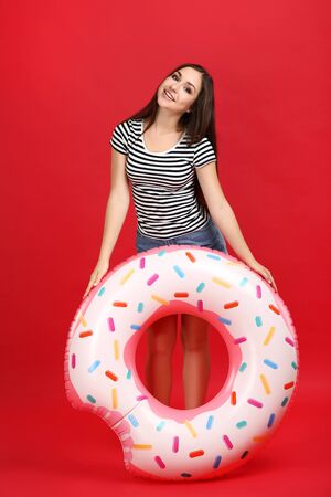 Young girl with inflatable donut on red backgroundの写真素材