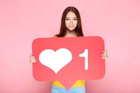 Young woman holding paper card with heart and number one on pink background