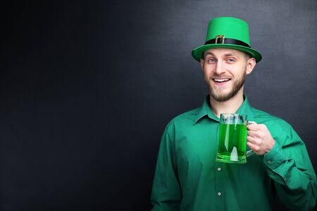 St. Patrick's Day. Young man wearing green hat with glass of beer on black background