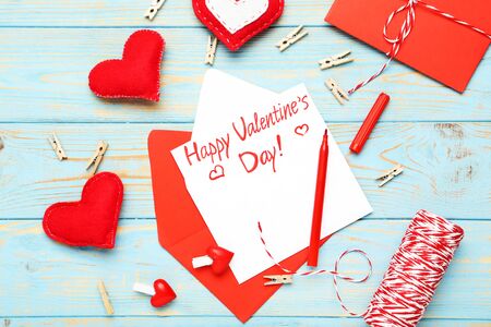 Paper envelope with fabric hearts, clothespins and text Happy Valentines Day on blue wooden tableの写真素材