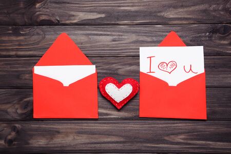 Red paper envelopes with fabric heart and text I Love You on wooden table