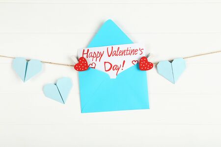 Paper envelope with hearts and text Happy Valentines Day hanging on white wooden backgroundの写真素材