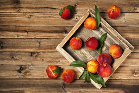 Fresh peaches with green leafs in crate on brown wooden tableの写真素材