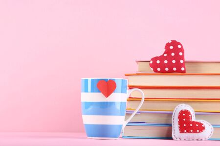 Fabric hearts with cup and stack of books on pink backgroundの写真素材