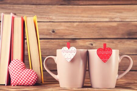 Fabric heart with cup, books and clothespins on brown wooden tableの写真素材